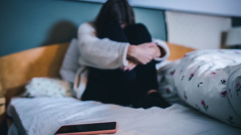 Una adolescente triste en su dormitorio con su teléfono móvil