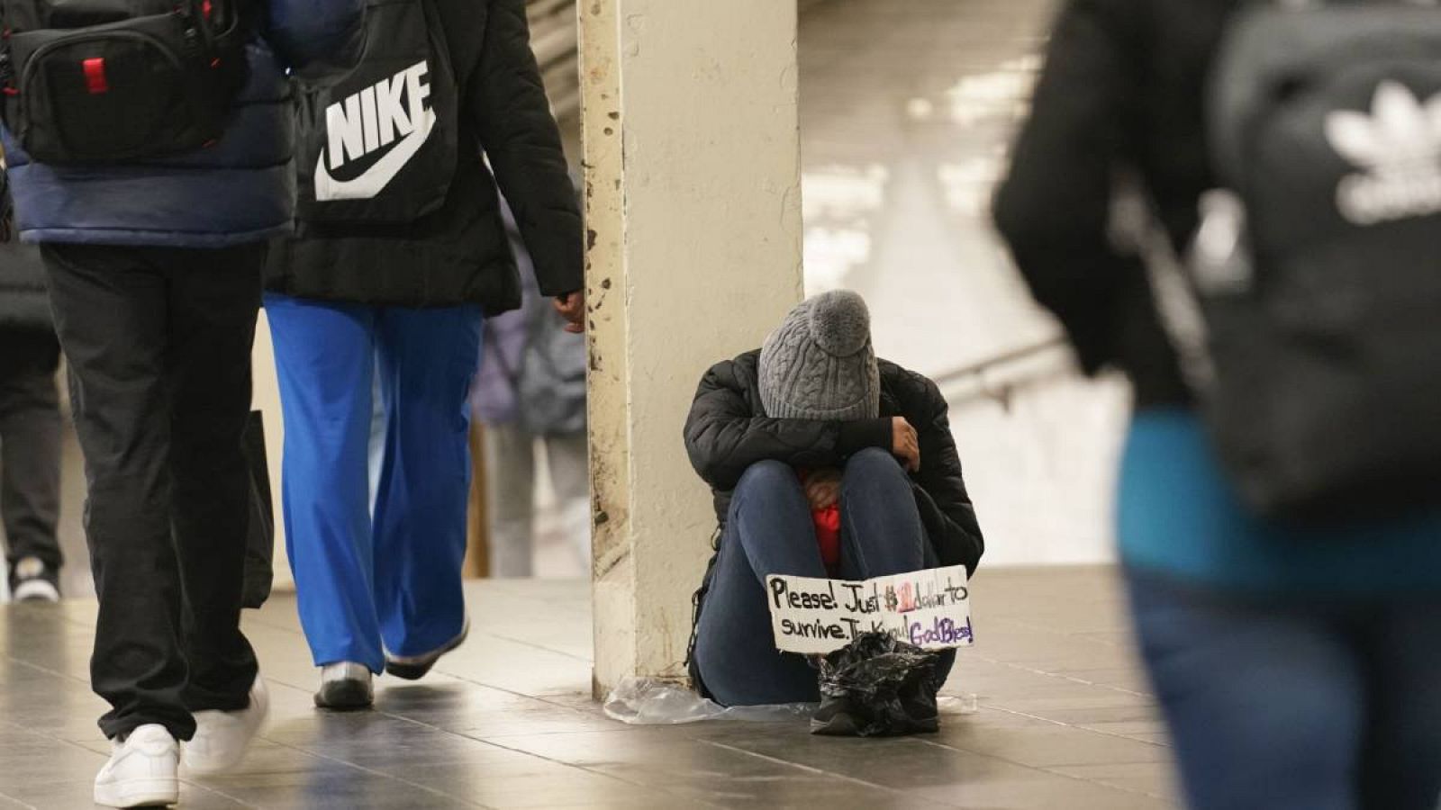 Una persona pide dinero con un cartel en una estación de metro de Nueva York, EE.UU.