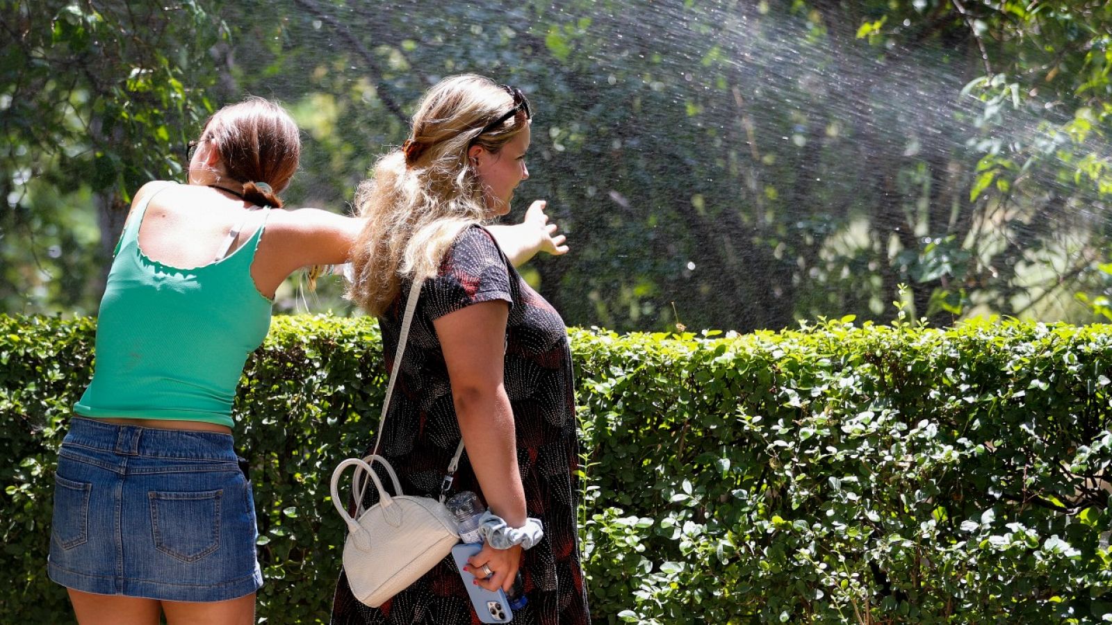 Dos mujeres se refrescan en un parque con el agua de un aspersor