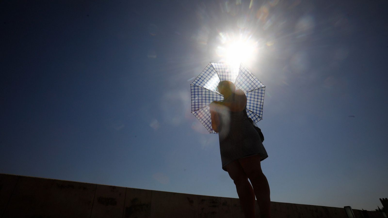 Una mujer se protege del sol con un paraguas mientras pasea por el puente romano de Córdoba