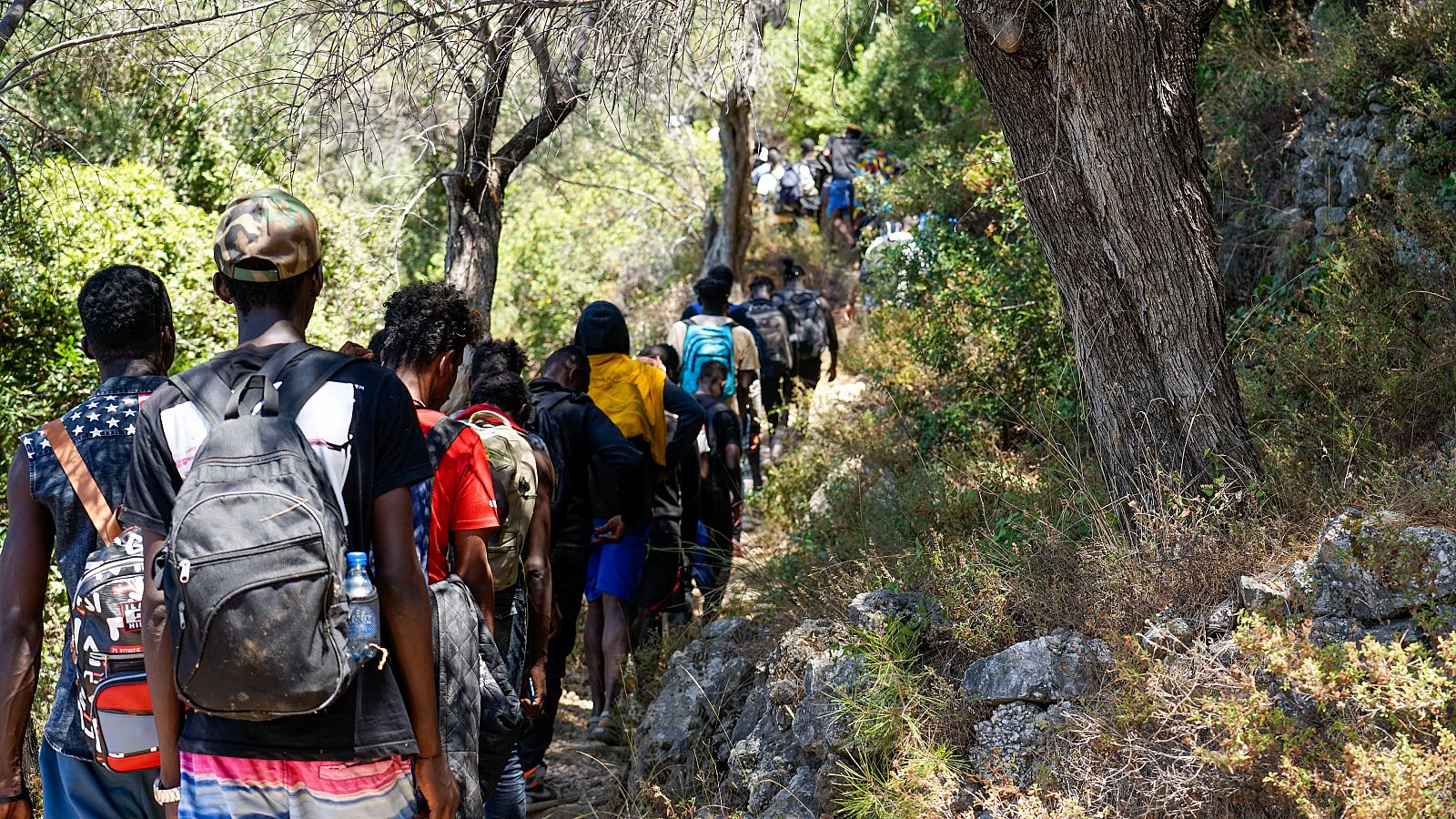 Plano medio de personas recién llegadas a la isla de Samos, Grecia, caminando por un sendero rocoso