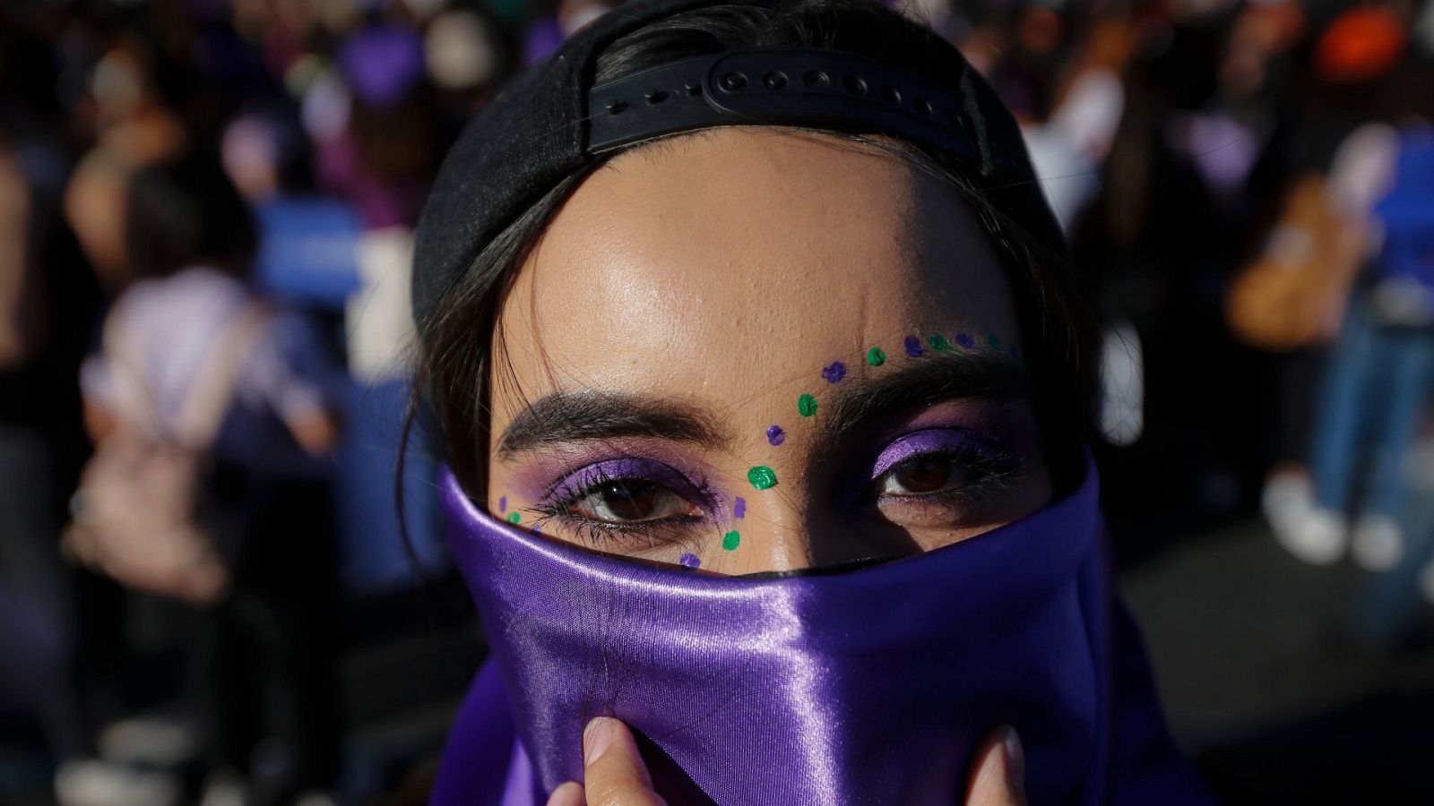 Una activista tapa su cara con un pañuelo violeta y lleva un maquillaje con puntos morados y verdes. Participa en una manifestación por el 8M en México