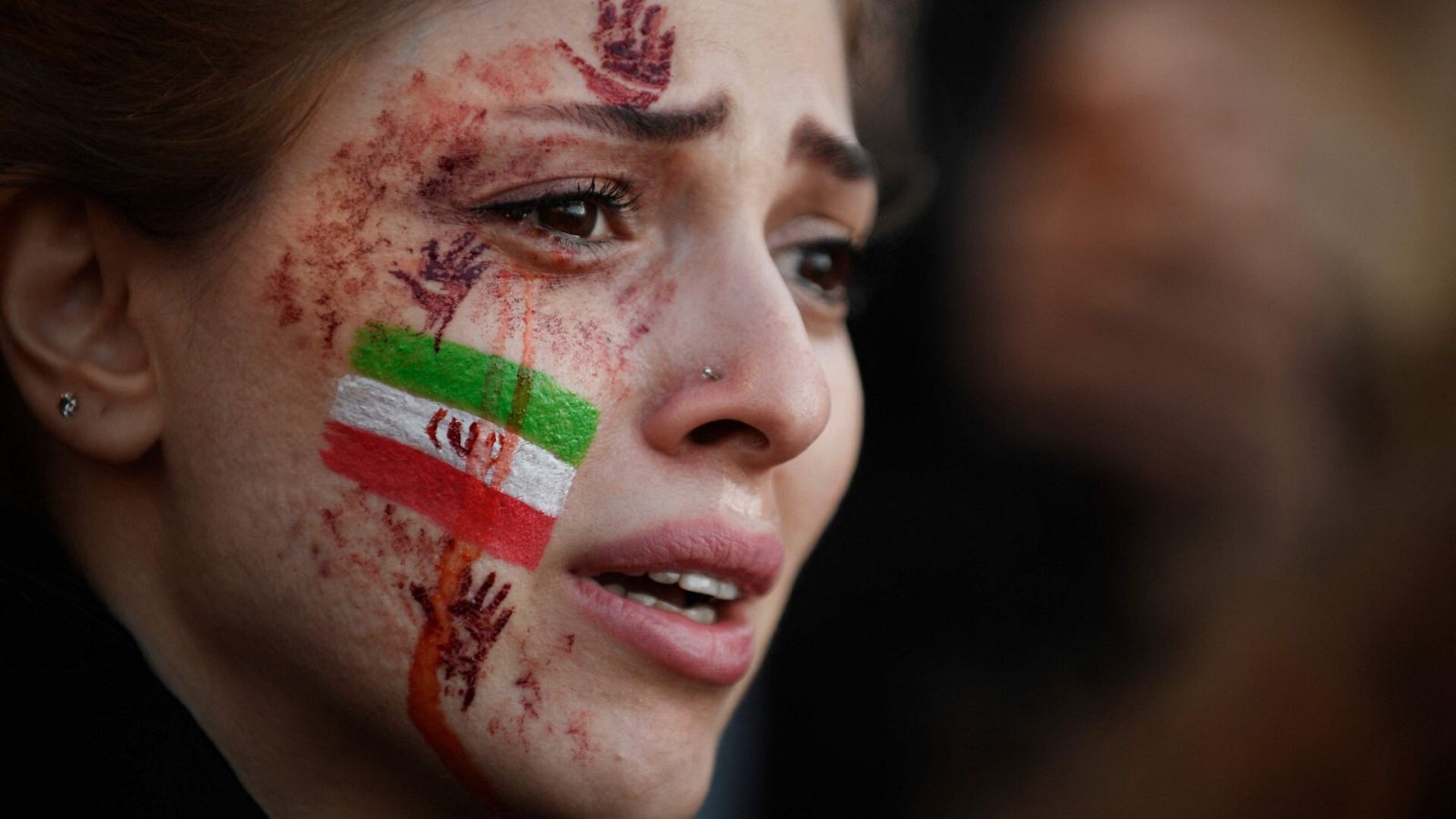 Una manifestante con una bandera iraní y manos pintadas de rojo en la cara