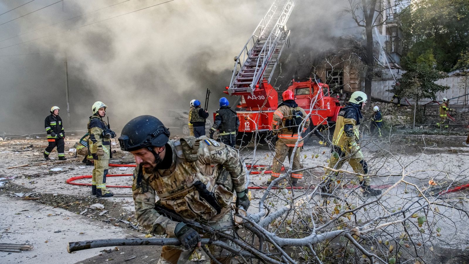 Los bomberos ayudan a una mujer a evacuar un edificio residencial destruido por un ataque con drones en Kiev