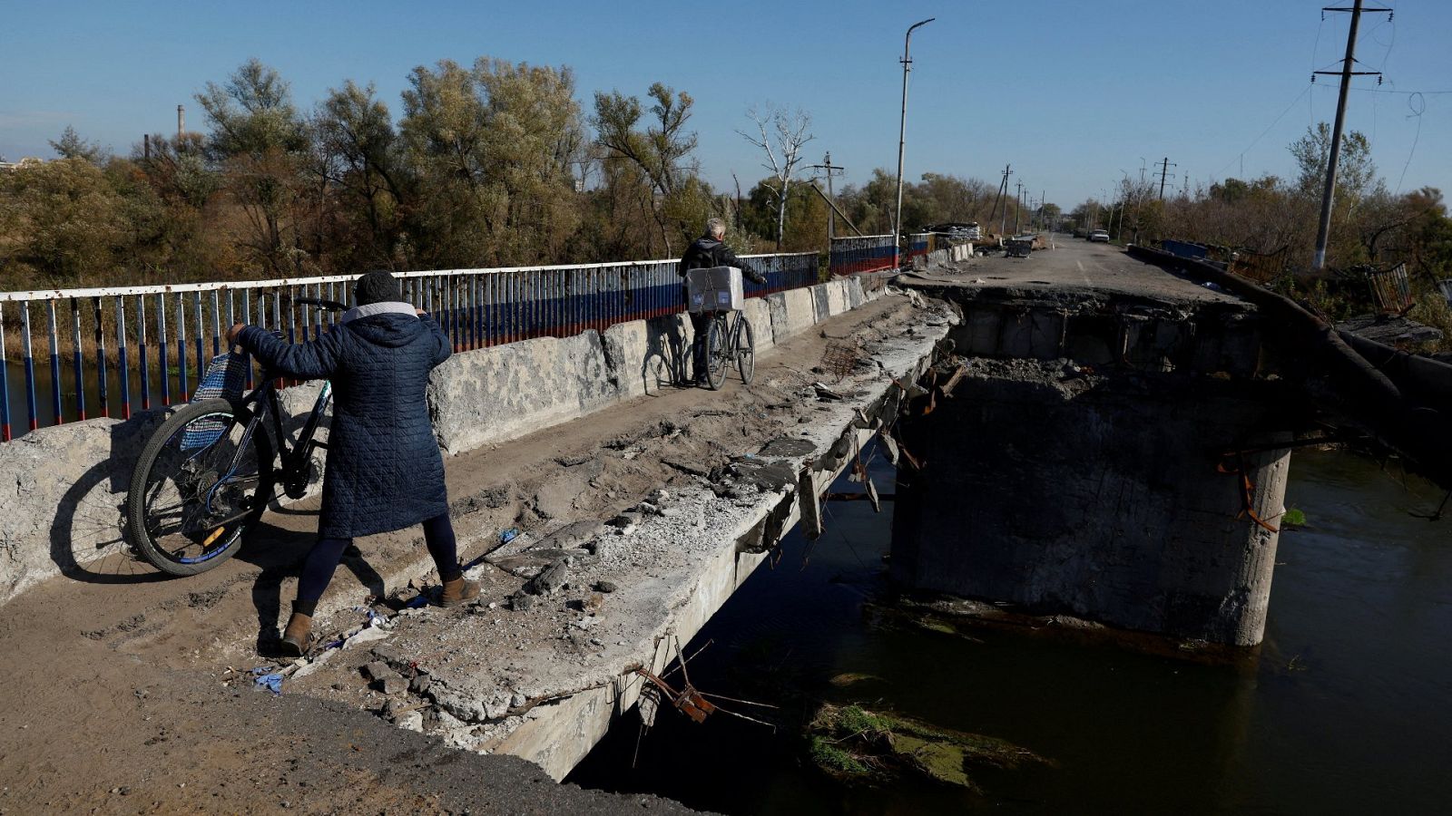 Una mujer empuja su bicicleta a lo largo de un puente destruido en Kupiansk, localidad retomada por Ucrania. 