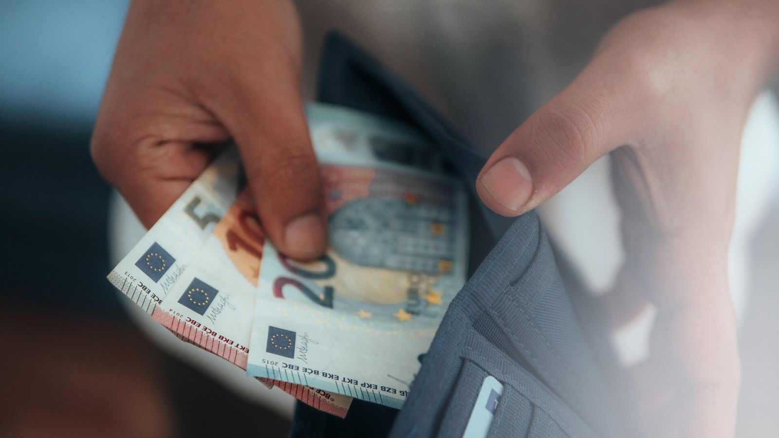 Un joven saca billetes de euro de la cartera