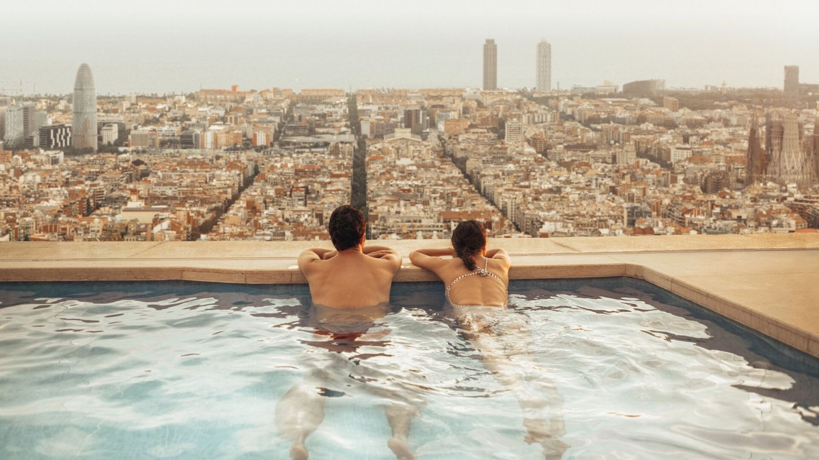 Una pareja mira a Barcelona desde la piscina de la azotea de un hotel
