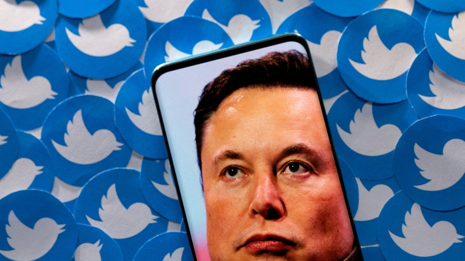 Fotomontaje de una imagen de Elon Musk en la pantalla de un smartphone que está sobre unos logotipos de Twitter.