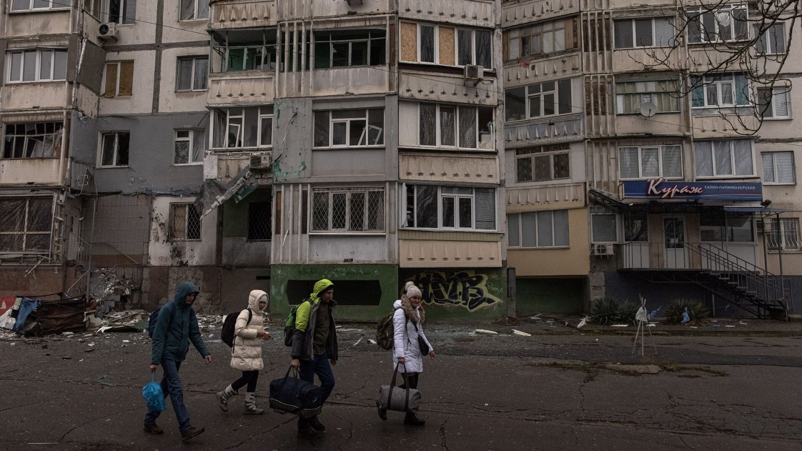 Varias personas con equipaje pasan frente a un edificio de viviendas dañado en la ciudad de Jersón