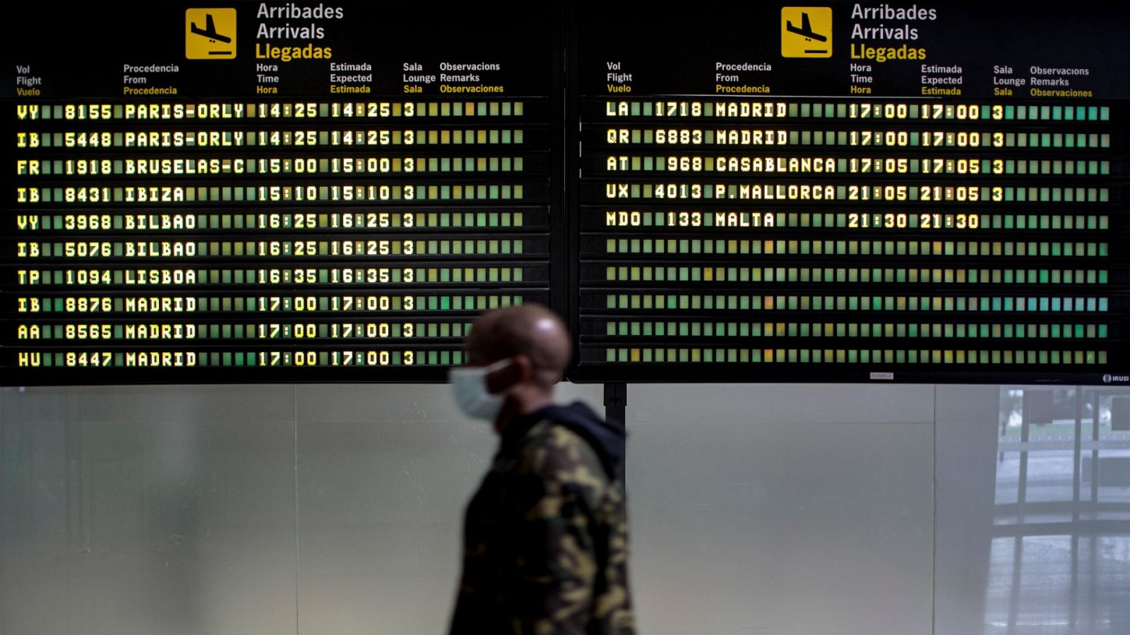 Un persona con mascarilla pasa frente al panel de llegadas del aeropuerto de València durante la pandemia de coronavirus