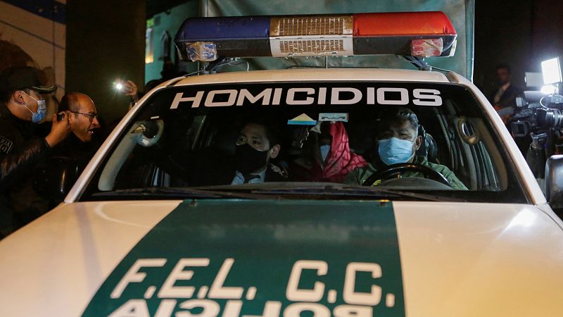 El gobernador opositor de Santa Cruz, Luis Fernando Camacho, se cubre la cara mientras es escoltado en un coche de policía