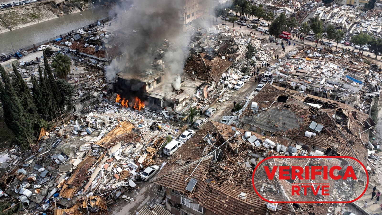 Fotografía del 7 de febrero 2023 que muestra un edificio en llamas entre otras construcciones derrumbadas después del terremoto en la provincia de Hatay (Turquía), con el sello 'VerificaRTVE' en rojo