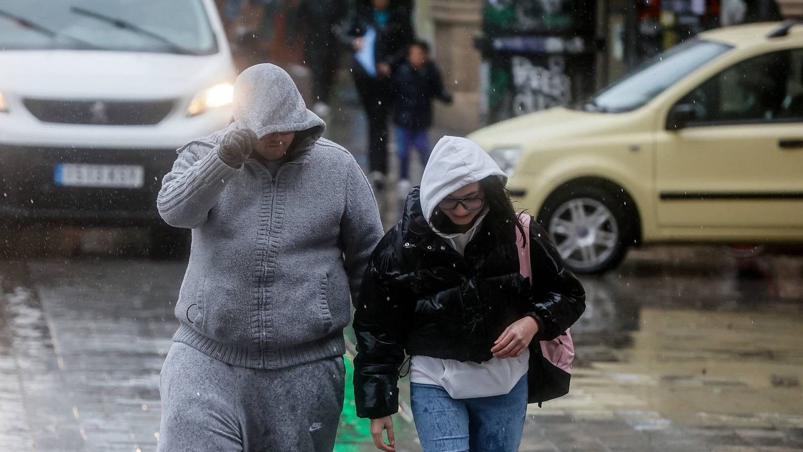 Dos personas se tapan la cabeza con la capucha de la chaqueta como consecuencia de la lluvia en Valencia en una imagen captada el pasado 6 de febrero