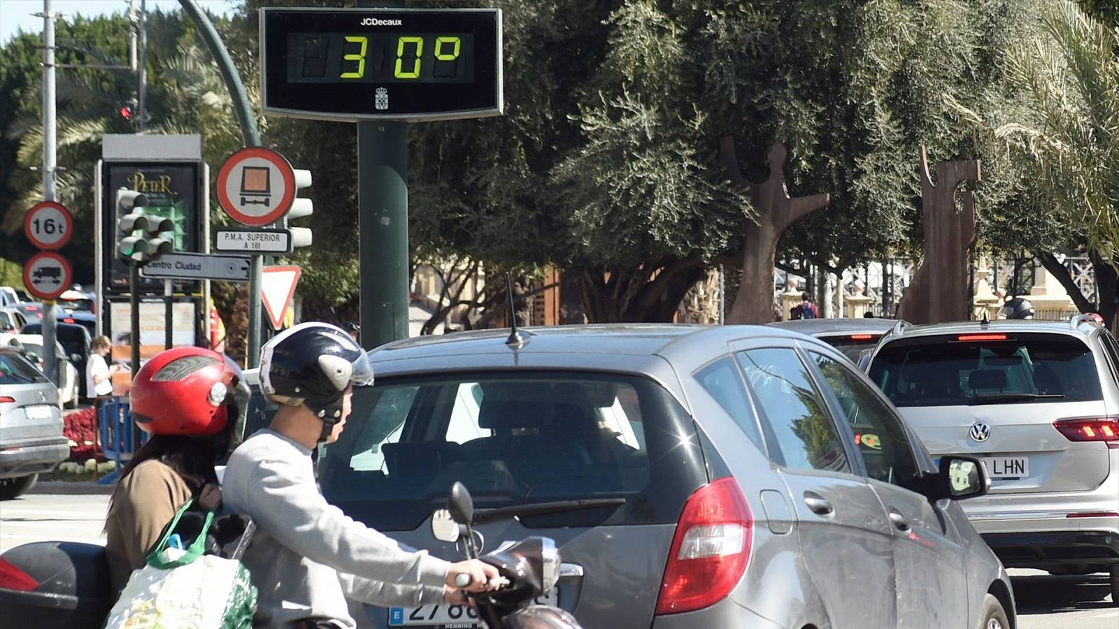 Una pareja en moto pasa cerca de un termómetro que marca los 30 grados el pasado 8 de marzo en Murcia