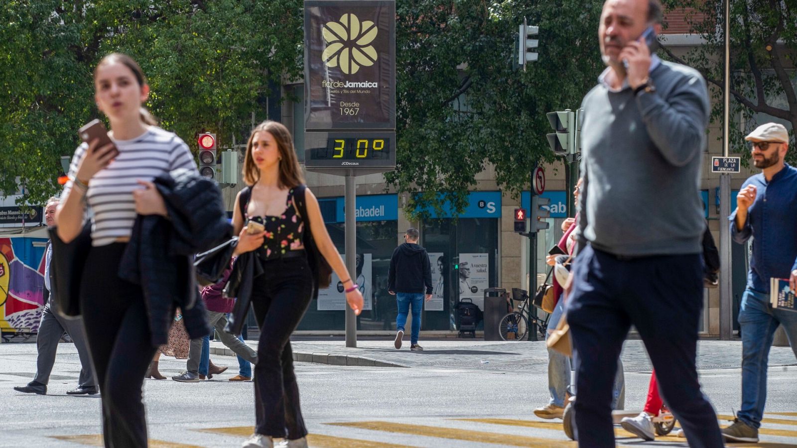 Suben las temperaturas: Varias personas cruzan un paso de peatones junto a un termómetro