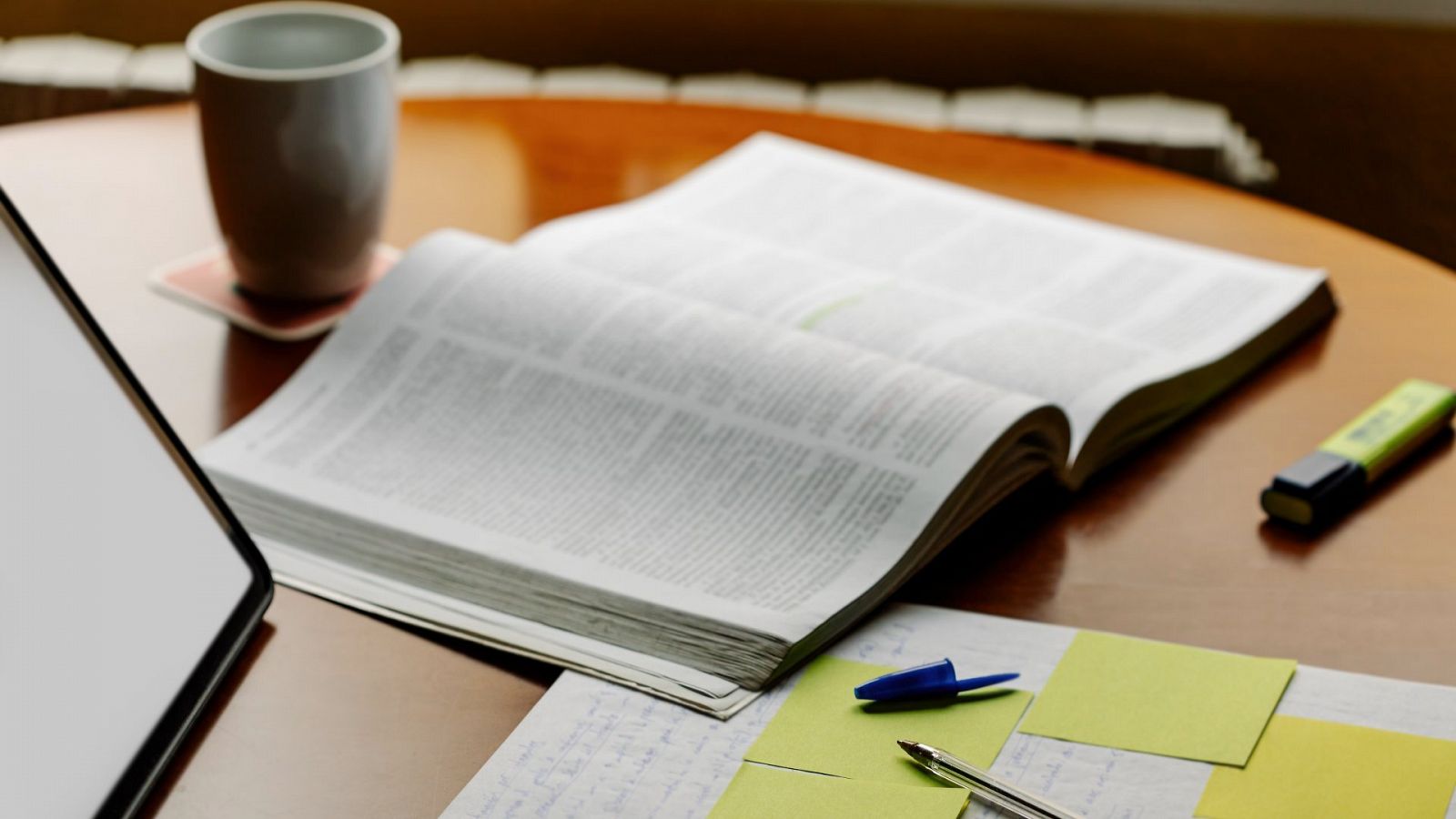 Un cuaderno con apuntes y subrayadores junto a una taza y sobre una mesa de escritorio.