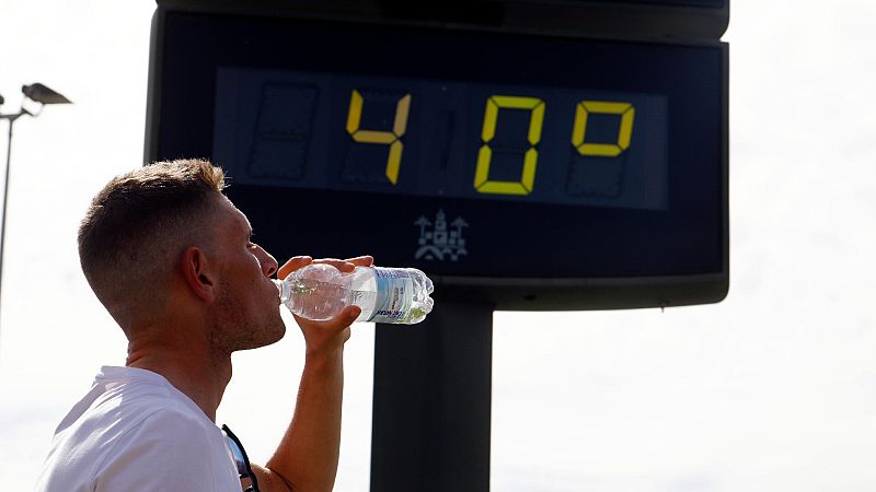 Un joven bebe agua junto a un termómetro de calle que marca 40 grados en el centro de Córdoba a finales de abril de 2023