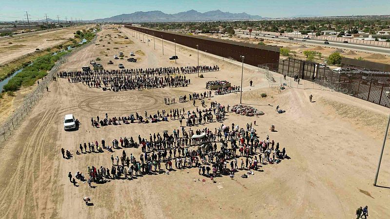 Cientos de migrantes mientras esperan junto al muro fronterizo en El Paso, en Texas, EE.UU.