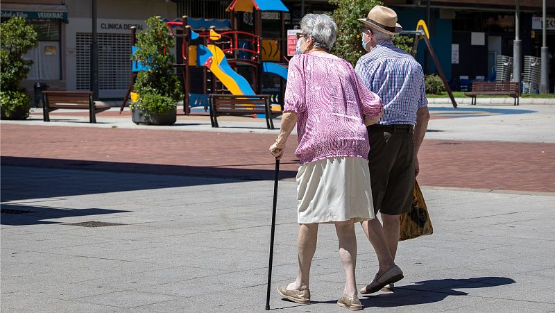 Una pareja de ancianos pasea agarrada del brazo y vestidos con ropa veraniega