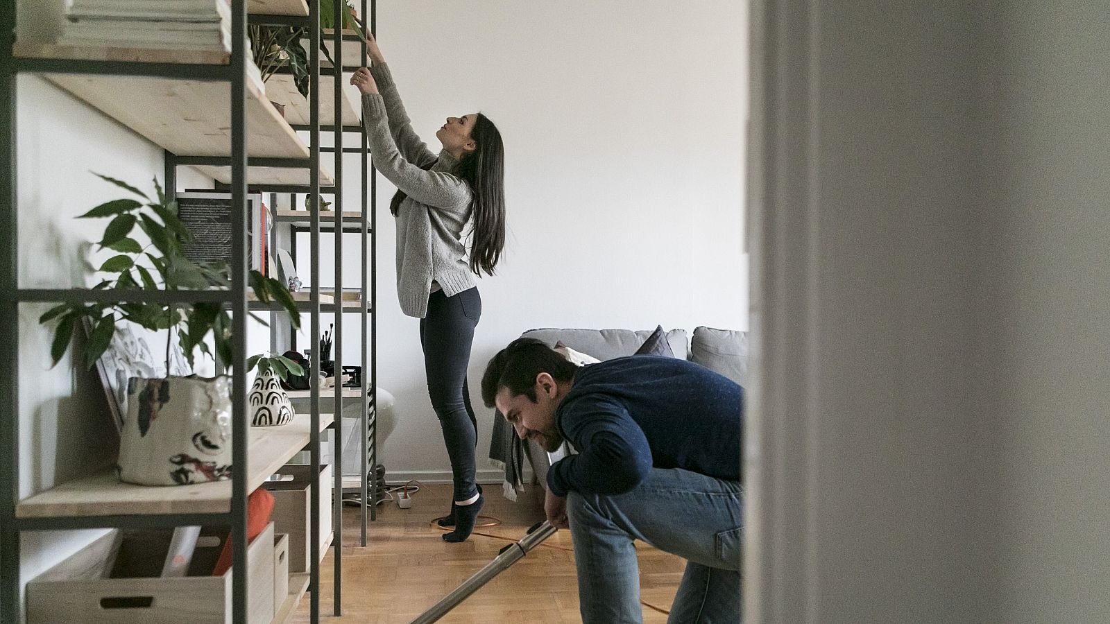 Un hombre aspira el suelo mientras una mujer limpia una estantería en casa