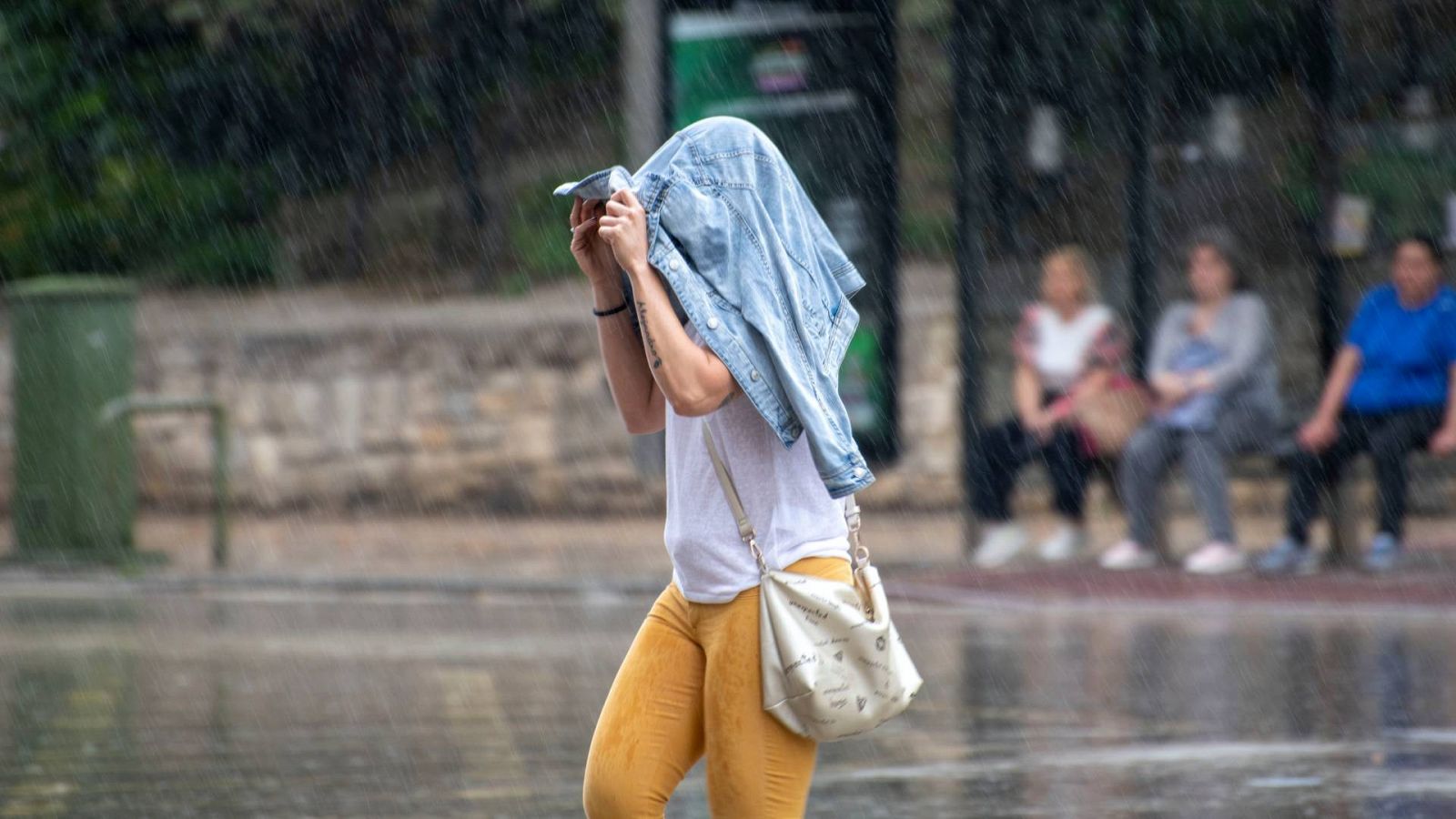 Una mujer se protege con la cazadora al comienzo súbito de la lluvia hoy en Jaén capital