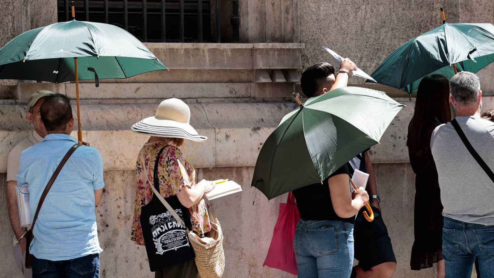 Varias personas que guardan cola en Valencia se protegen del sol