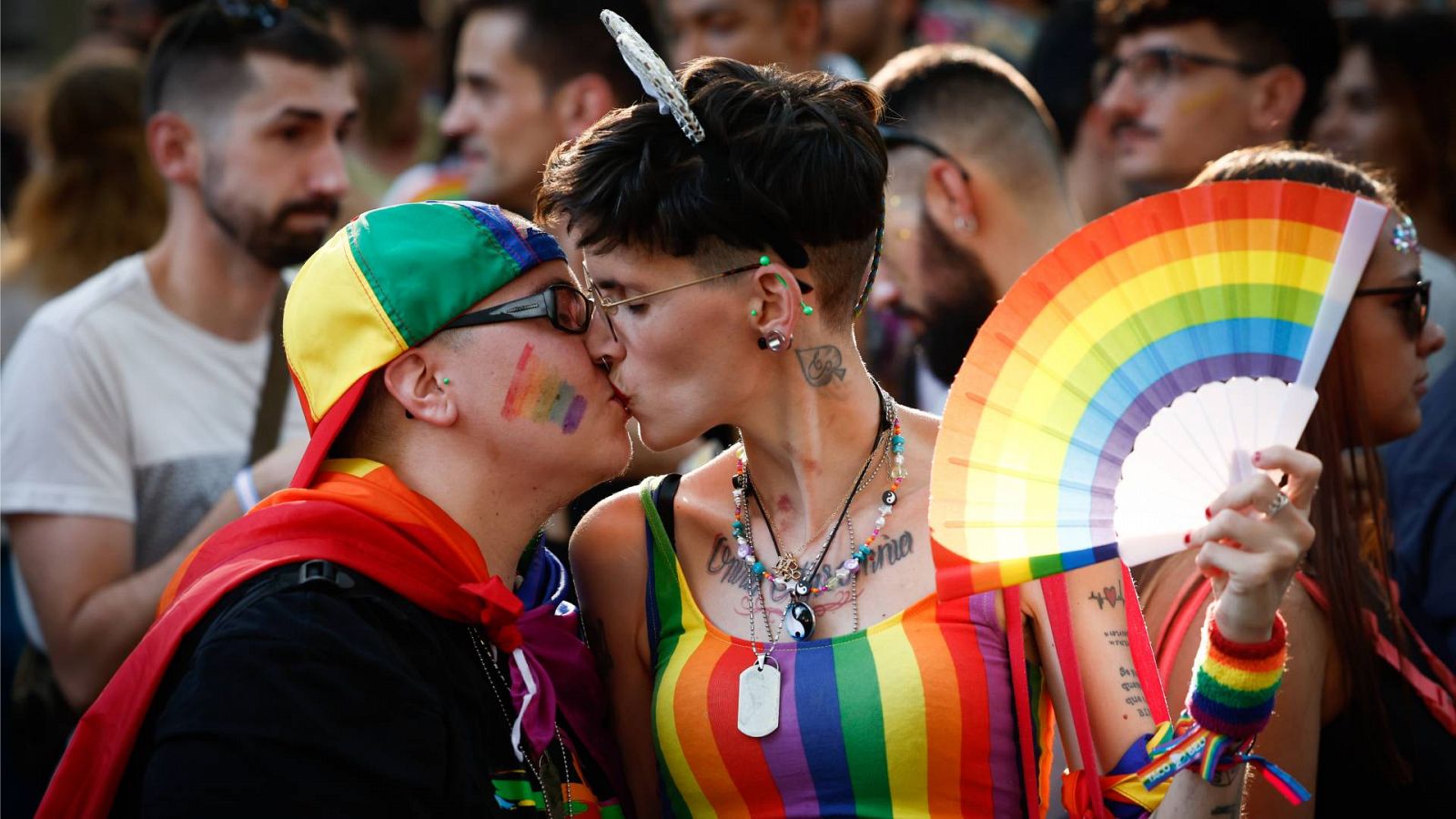 Orgullo LGTBI 2023: calendario, actividades y actos: Dos personas vestidas con la bandera LGTBI+ besándose durante la marcha del Orgullo 2022 en Madrid