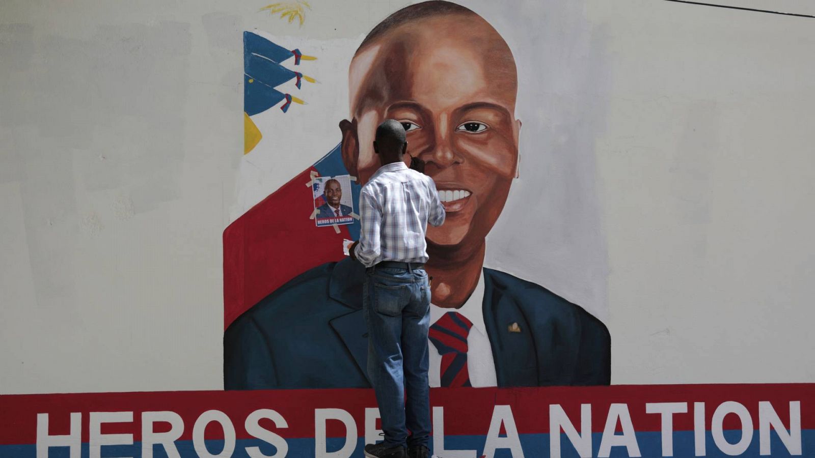 Un hombre pintando en una pared de una calle de Puerto Principe un retrato de Jovenel Moise.