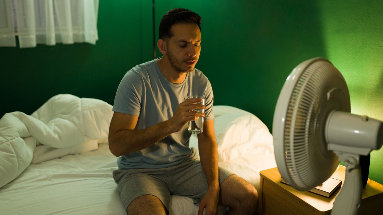 Las altas temperaturas son más peligrosas por las noches: Un hombre bebe agua mientras utiliza un ventilador en su dormitorio