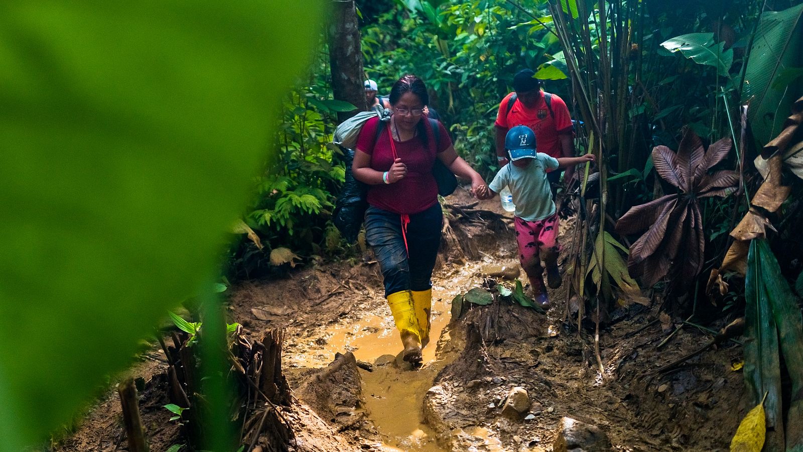 Una migrante ecuatoriana y su hija vestida con ropa de niño caminan por un sendero embarrado en la selva del Darién