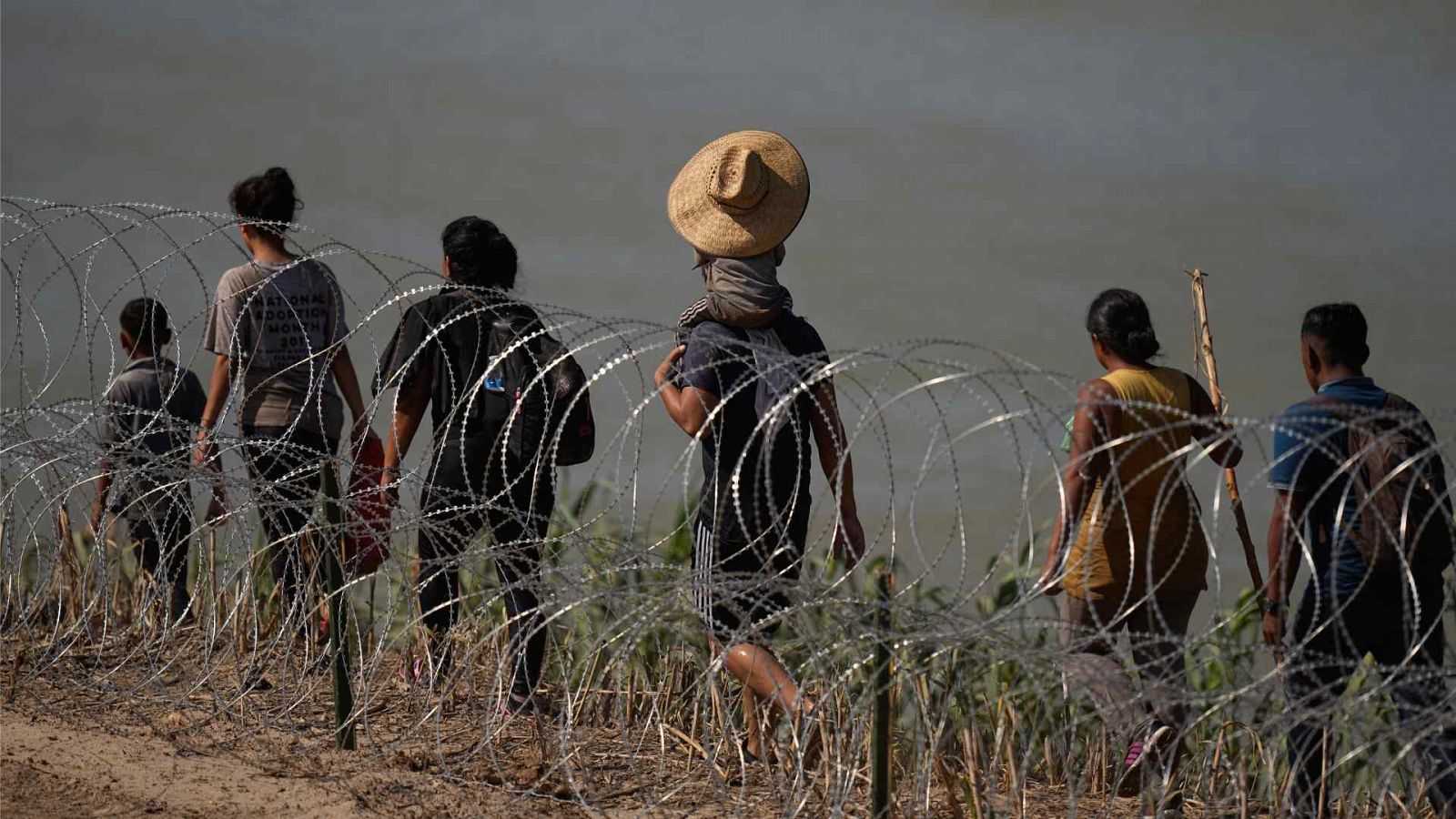 Migrantes caminan a lo largo del alambre de concertina en el río Grande mientras tratan de entrar en los EE.UU. desde México.