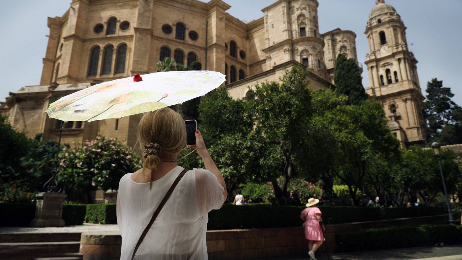 Una joven se protege del calor mientras hace una fotografía de la catedral de Málaga