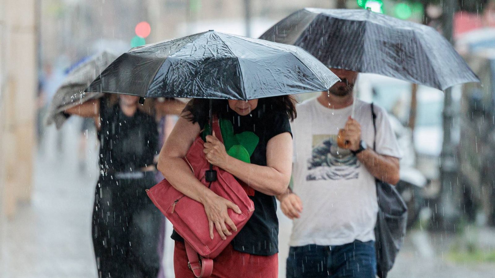 Tres personas caminando con paraguas bajo la lluvia