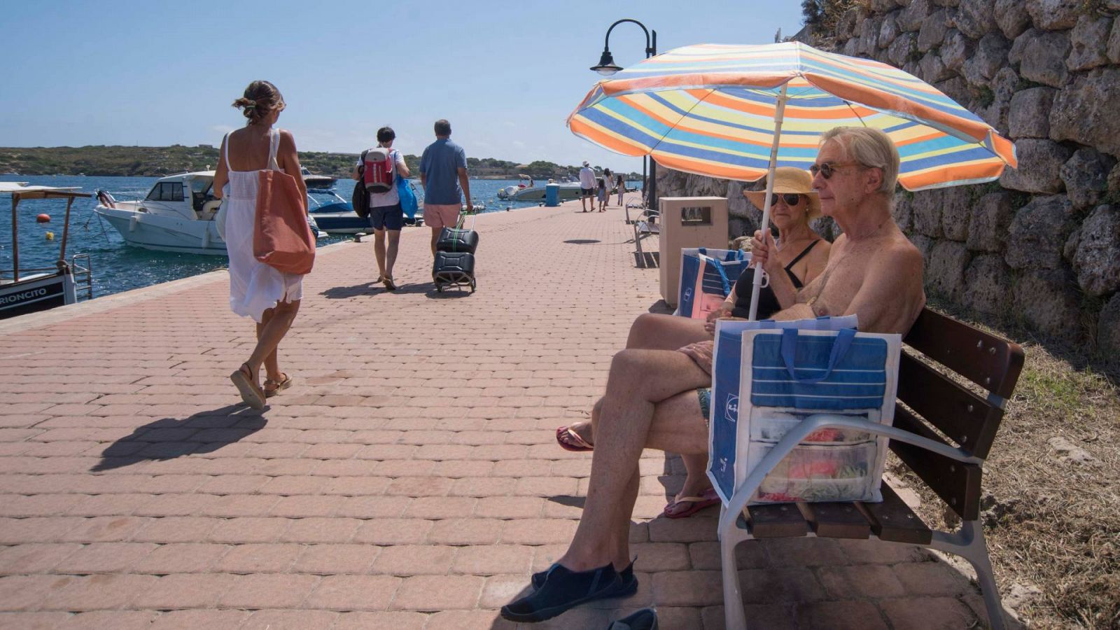 Un hombre y una mujer se protegen con una sombrilla del sol en el Moll d'en Pons, Menorca