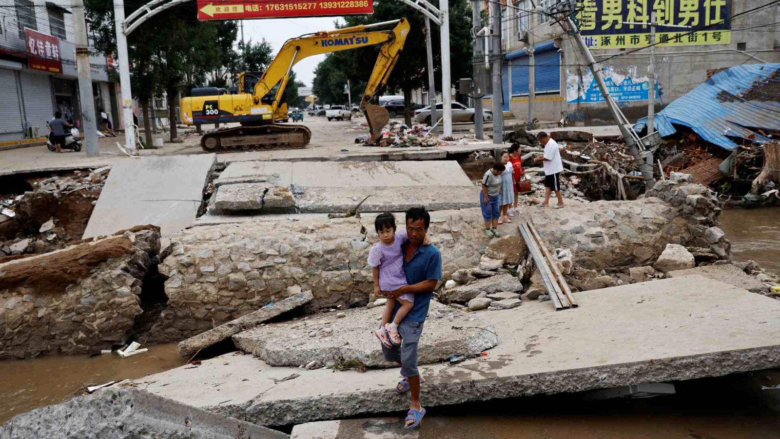 Un hombre con un niño en brazos camina por un puente dañado tras las lluvias e inundaciones provocadas por el tifón Doksuri, en Hebei, China.