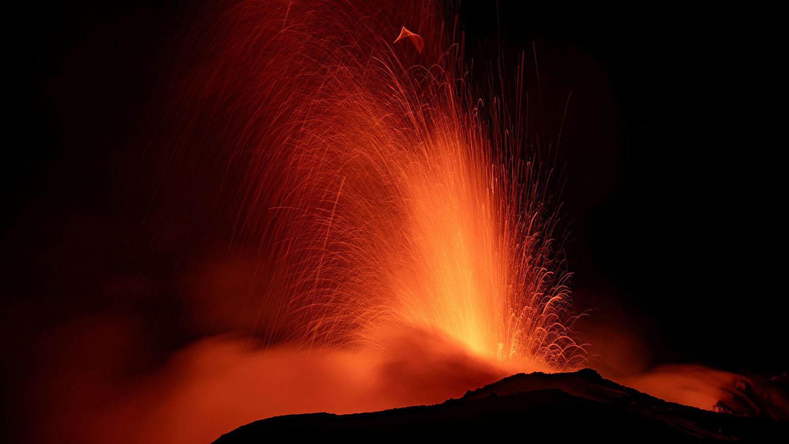 Imagen nocturna de lava saliendo del cráter del volcán como fuego.