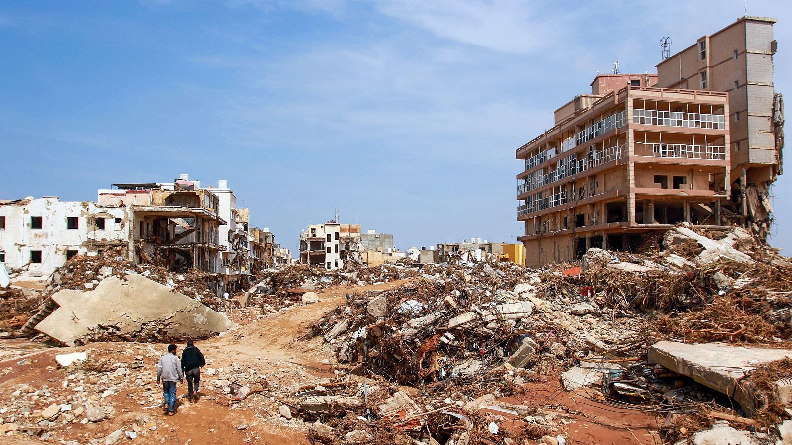 Unos hombres caminan junto a los escombros de los edificios causados por las inundaciones en Derna