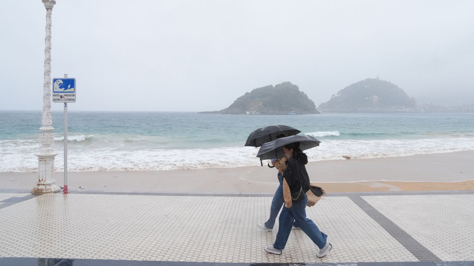 Dos personas con paraguas en la playa de Ondarreta, Guipúzcoa