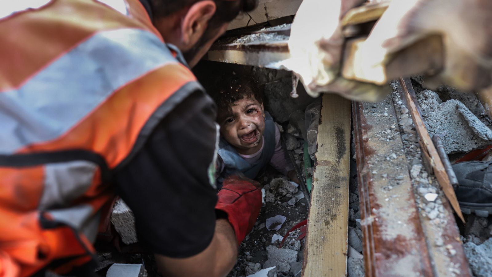 Los palestinos rescatan a una niña pequeña de debajo de los escombros de un edificio destruido tras un ataque aéreo israelí en la ciudad de Gaza