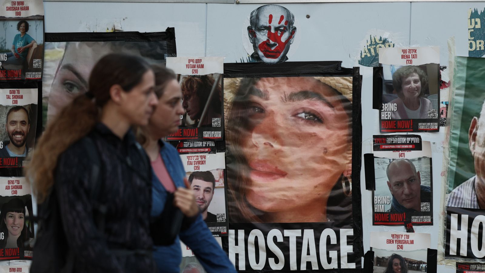 Dos personas caminan delante de las imágenes de los secuestrados por Hamás.