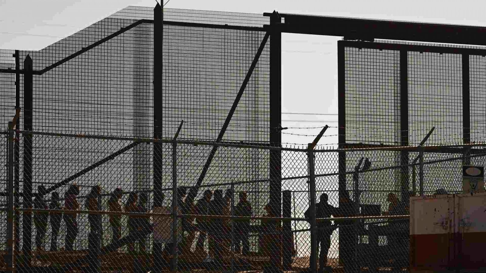Migrantes esperan junto al muro fronterizo en la puerta 42 para entregarse a los agentes de la Patrulla Fronteriza de Aduanas y Protección Fronteriza (CBP) de EE.UU.
