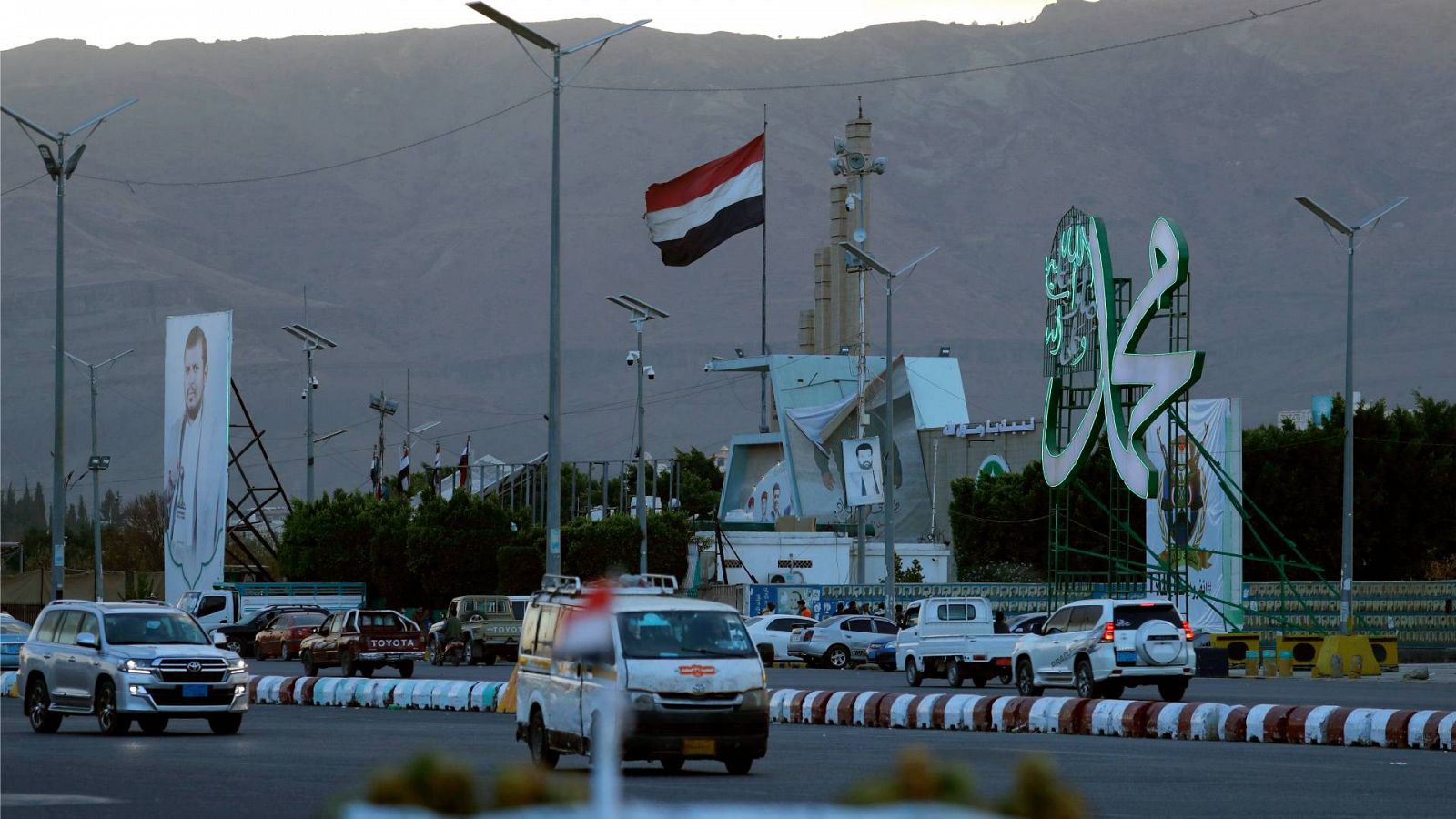 Una bandera yemení ondea mientras varios vehículos circulan por una calle en Saná, Yemen