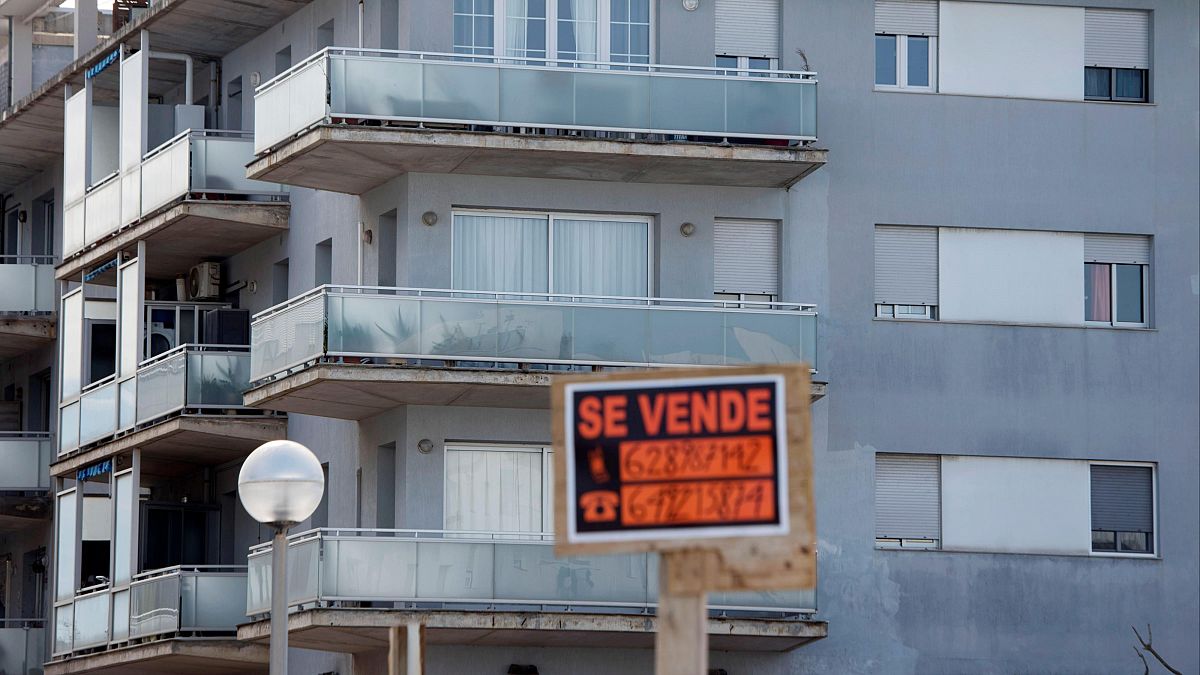 Fachada de edificio de apartamentos en venta; balcones con persianas, cartel naranja con dos números de teléfono y superficie (62 m²).