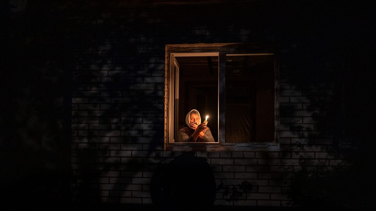 Una mujer sostiene una vela en la ventana de su casa durante un corte de energía en la región de Kiev