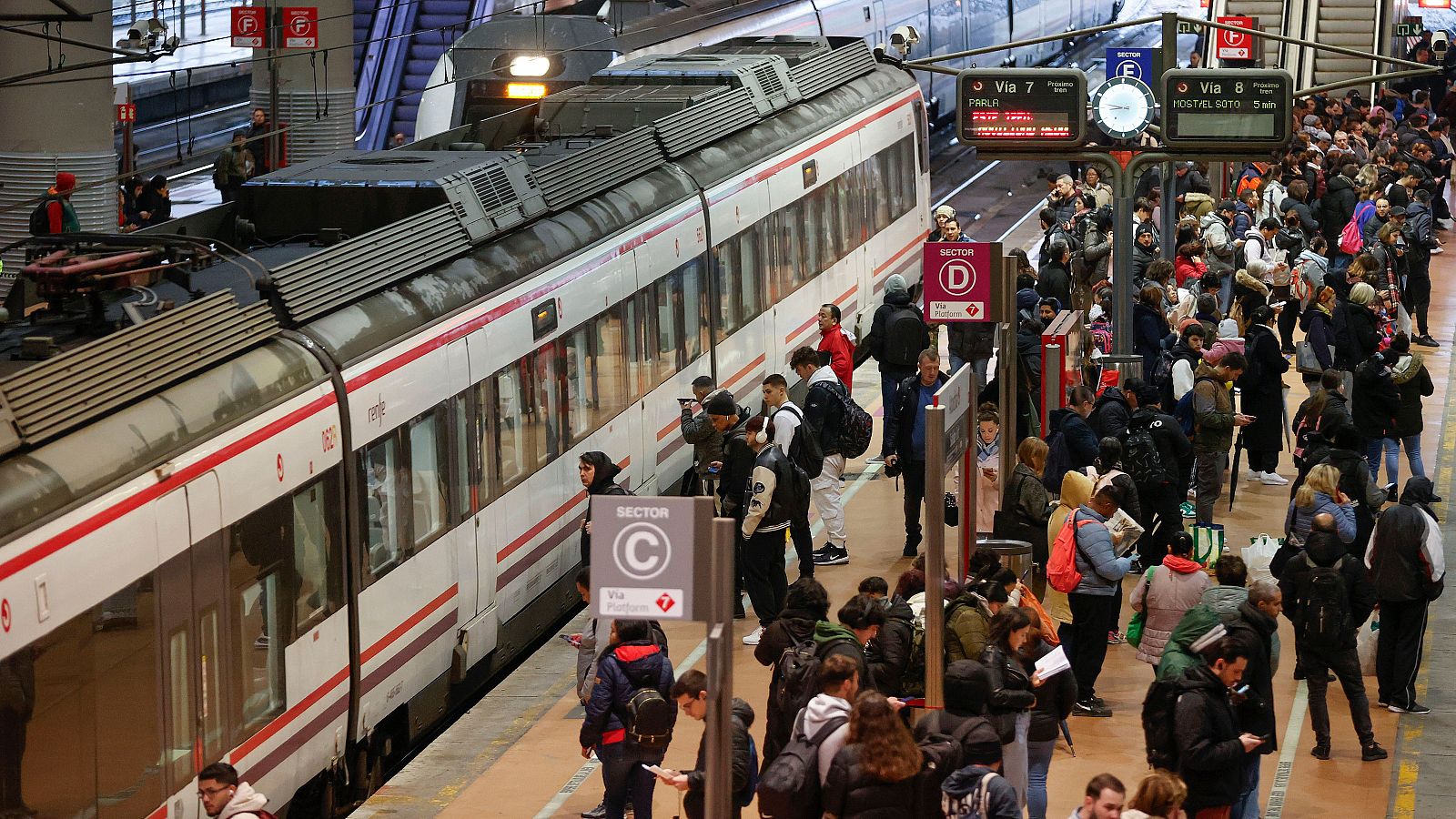 Varias personas esperan la llegada de un tren de Cercanías en la estación de Atocha