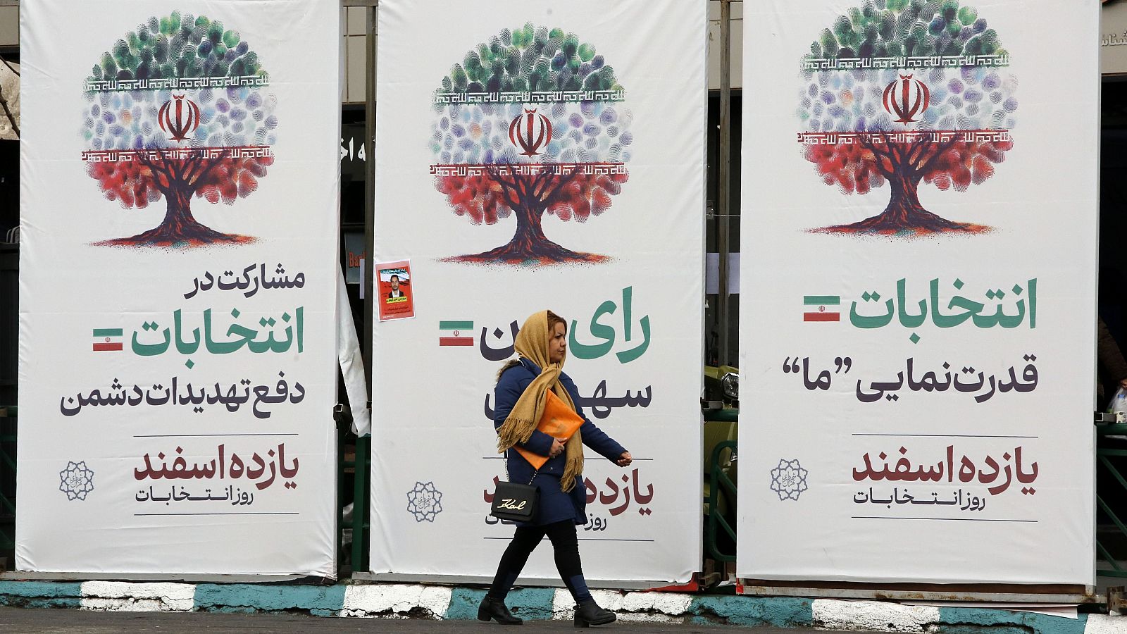 Una mujer iraní pasa por unos carteles electorales en la plaza Enghelab, en Teherán