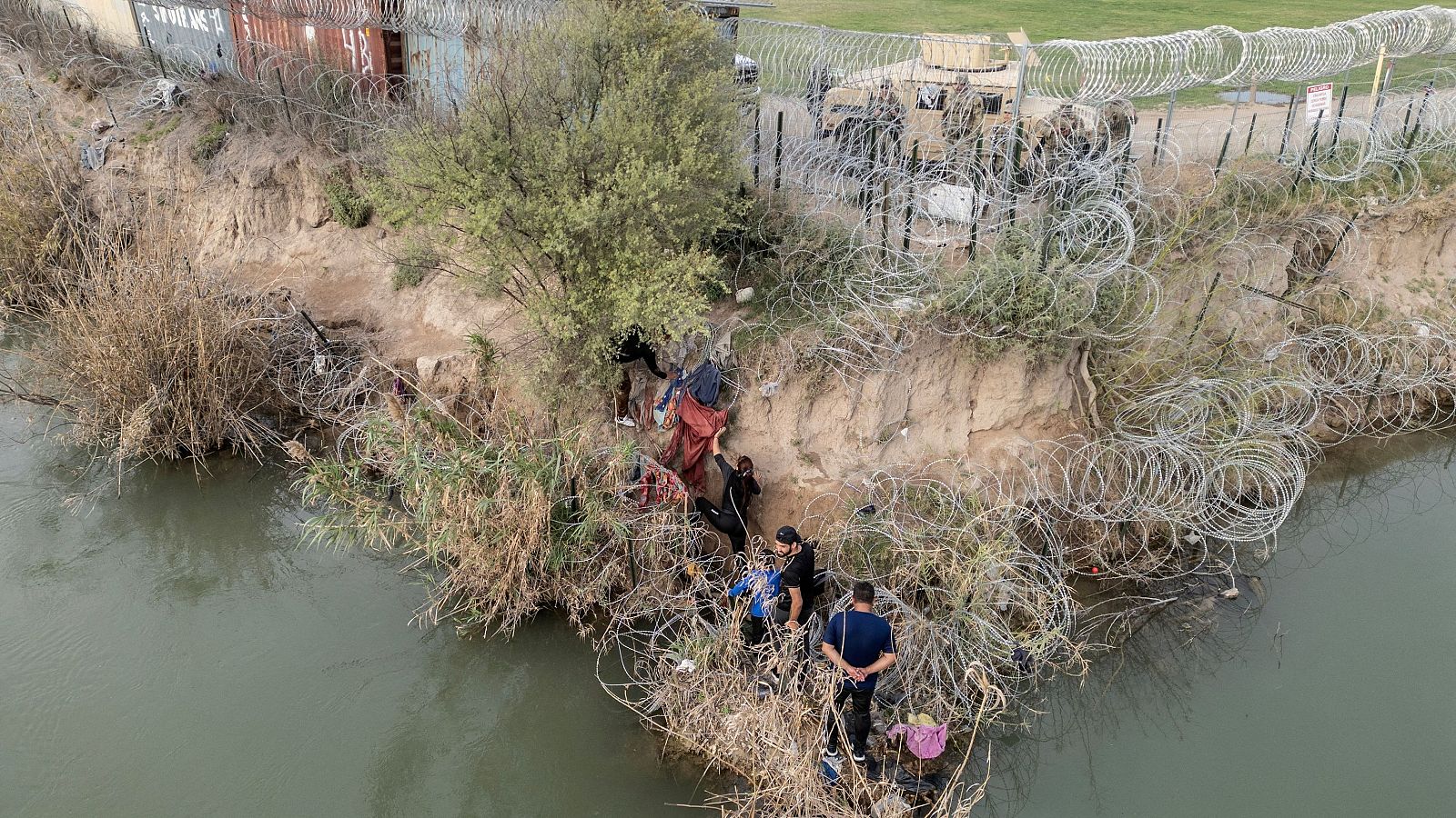 Un grupo de migrantes intenta atravesar una valla de alambre a orillas del río Grande mientras miembros de la Guardia Nacional de Estados Unidos vigilan al otro lado de la valla en Eagle Pass