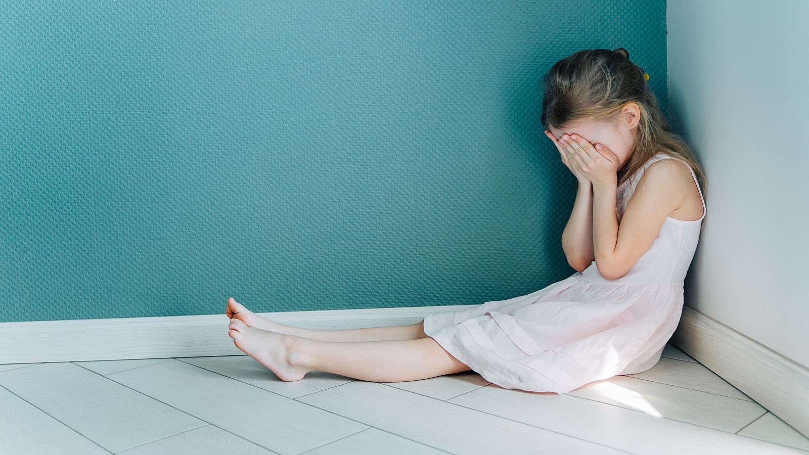Una niña llorando en la esquina de su habitación