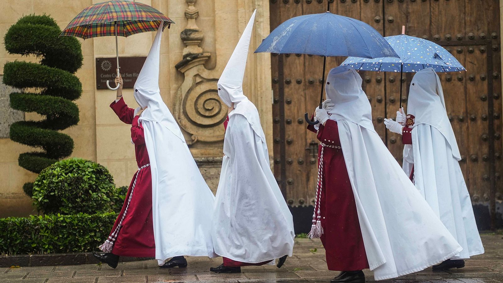 Unos nazarenos de la Hermandad de La Sentencia se protegen de la lluvia con paraguas en Córdoba
