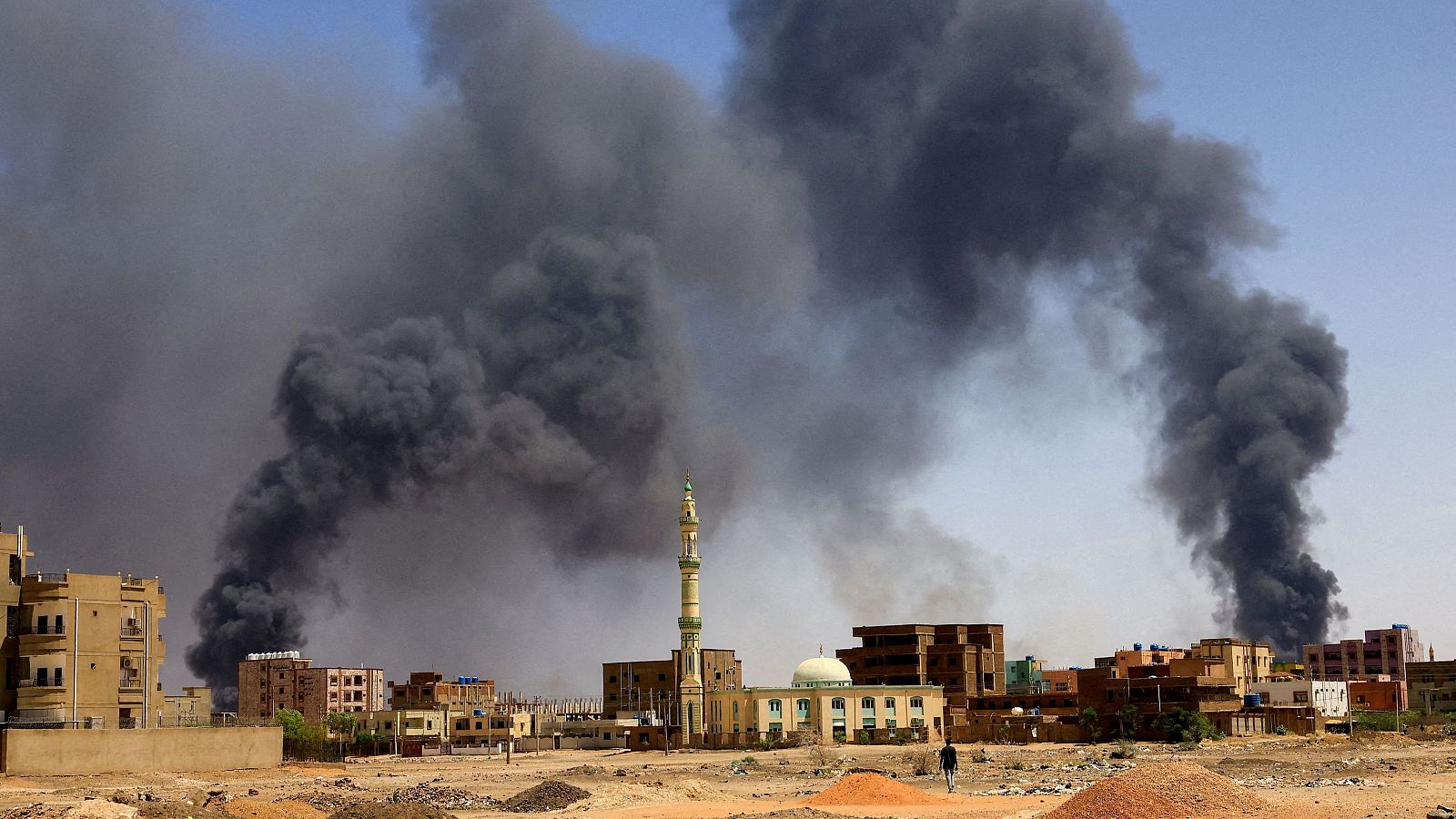 Un hombre camina mientras se eleva humo sobre los edificios tras un bombardeo aéreo en Jartum Norte